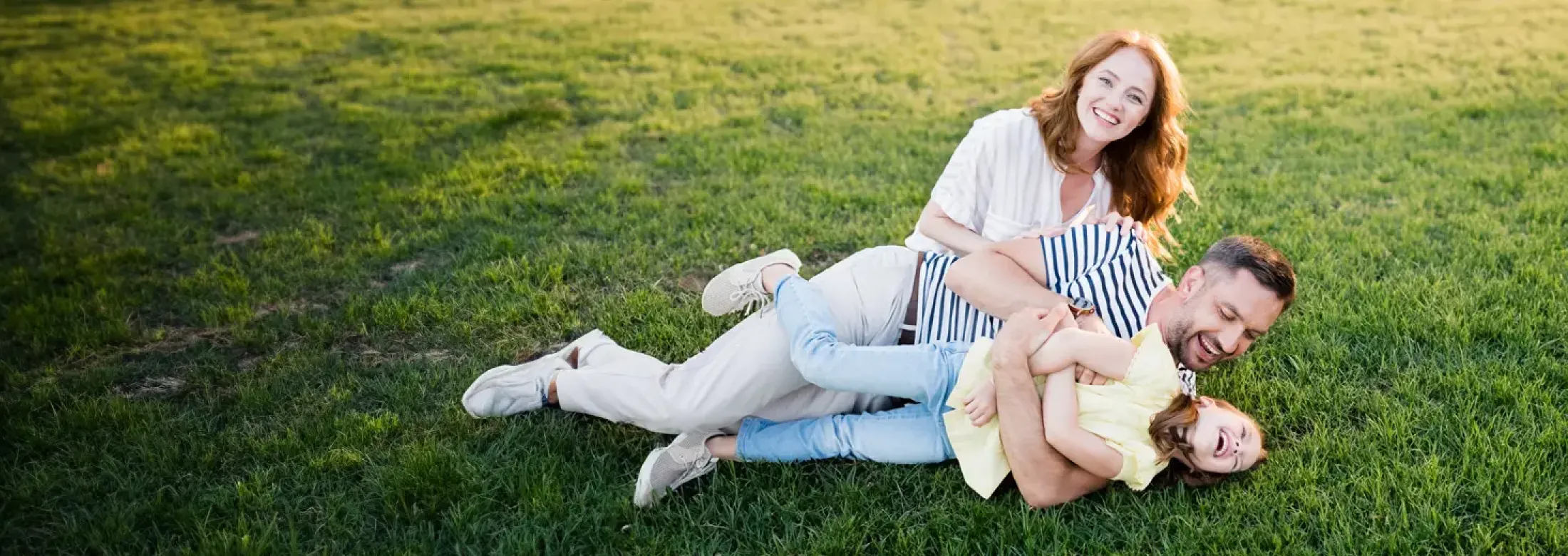 mom, dad, and daughter laughing outside laying in grass