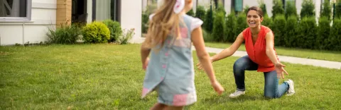 Mother and daughter playing outside on green healthy lawn