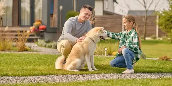 father and daughter petting dog on green healthy lawn
